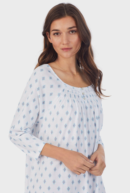  A lady wearing white long sleeve cotton waltz nightgown with aqua geo print. 